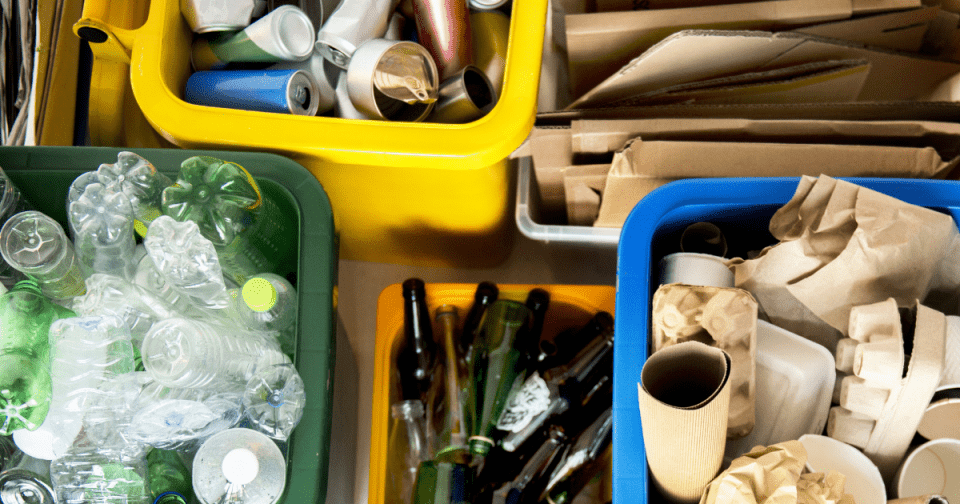 Image of recycling bins with materials separated by plastic, aluminum, glass, and cardboard 